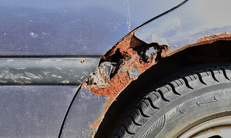 Sinisessä autossa on lokasuojassa ruostevaurio ja siitä puuttuu metallia